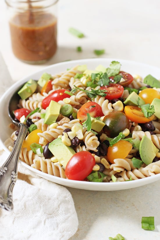 Side angle view of Vegetable Taco Pasta Salad in a bowl with a serving spoon and white napkin.