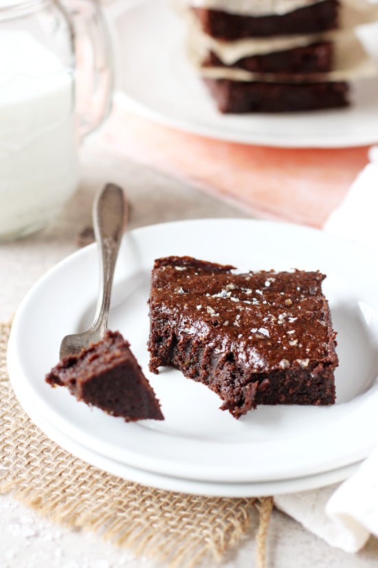 A Dark Chocolate Avocado Brownie on a plate with a bite taken out with a fork.