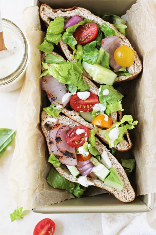 Grilled Greek Salad Pita Sandwiches stacked in a loaf pan with tahini sauce to the side.