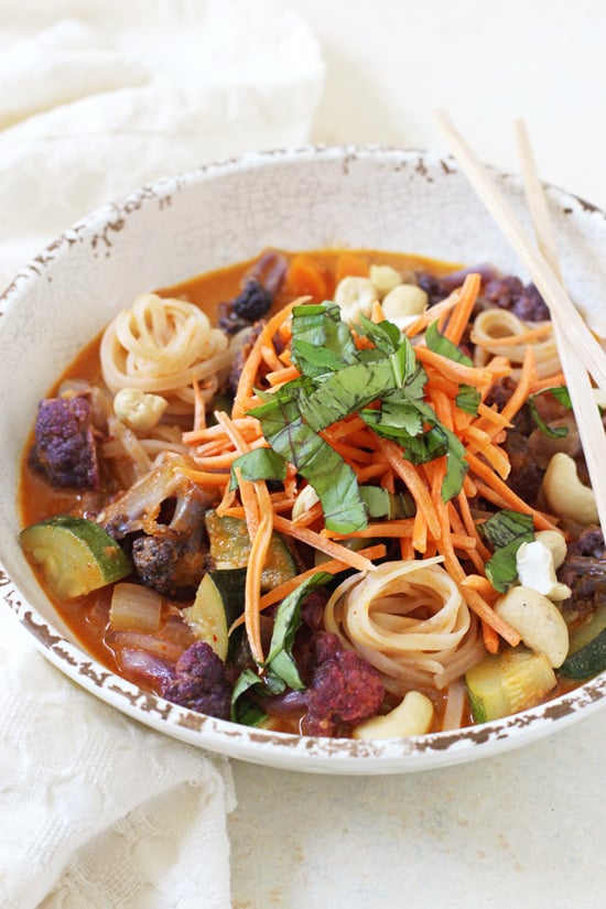 A side angle view of a Rainbow Vegetable Curry Noodle Bowl with chopsticks and a white napkin.