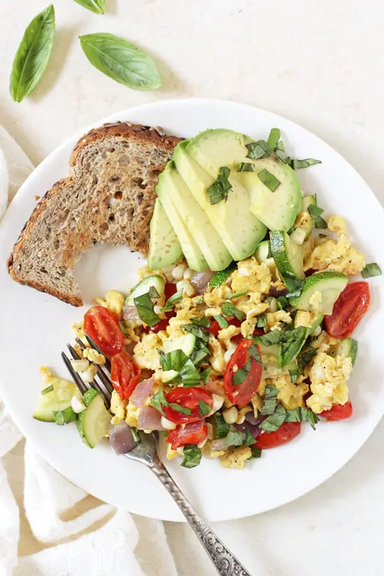 Summer Veggie Egg Scramble on a plate with a piece of bread and sliced avocado.