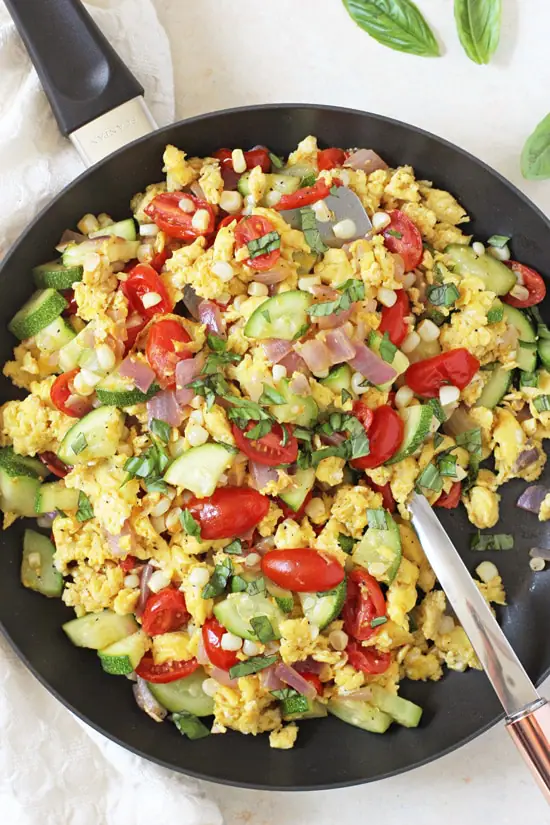 A skillet filled with Summer Veggie Egg Scramble and a serving spoon.