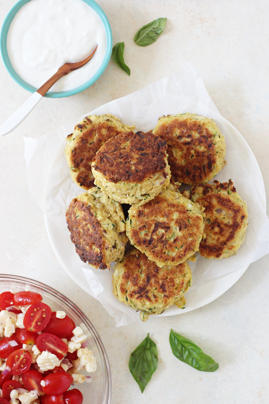 Healthy Zucchini Fritters stacked on a plate with yogurt and corn salsa in bowls to the side.