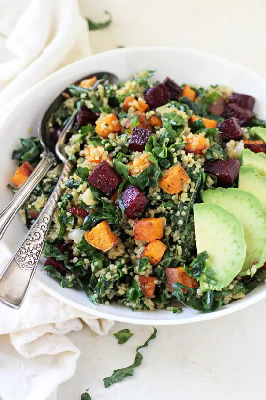 Side angle view of Kale and Quinoa Rainbow Salad in a bowl with a fork and spoon.