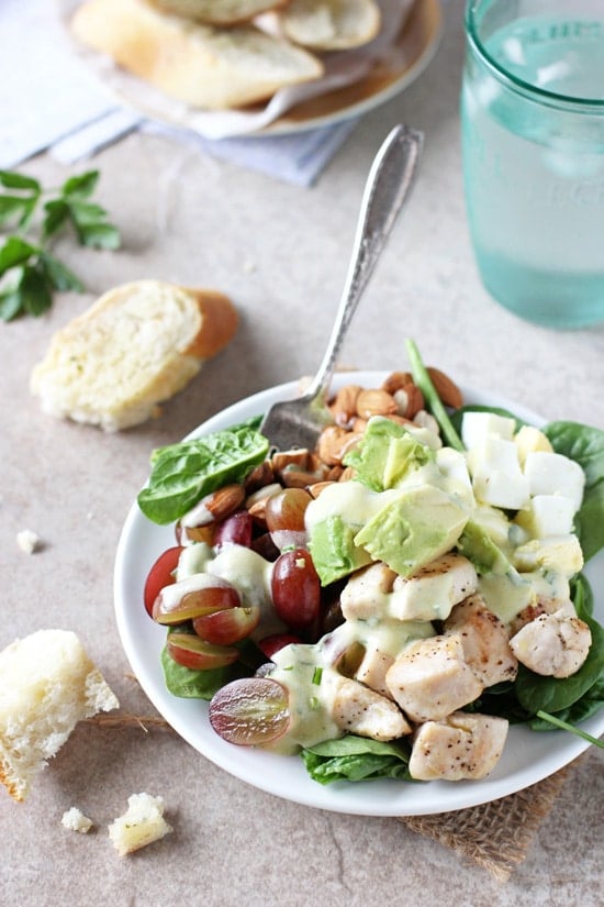 A white plate filled with Spinach Power Salad with a fork and water and bread to the side.