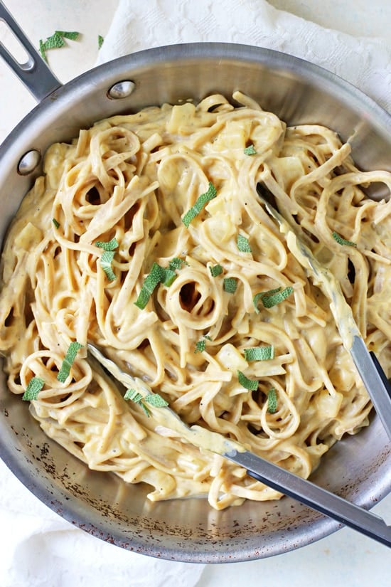 An all-clad skillet with Vegan Pumpkin Alfredo and tongs.