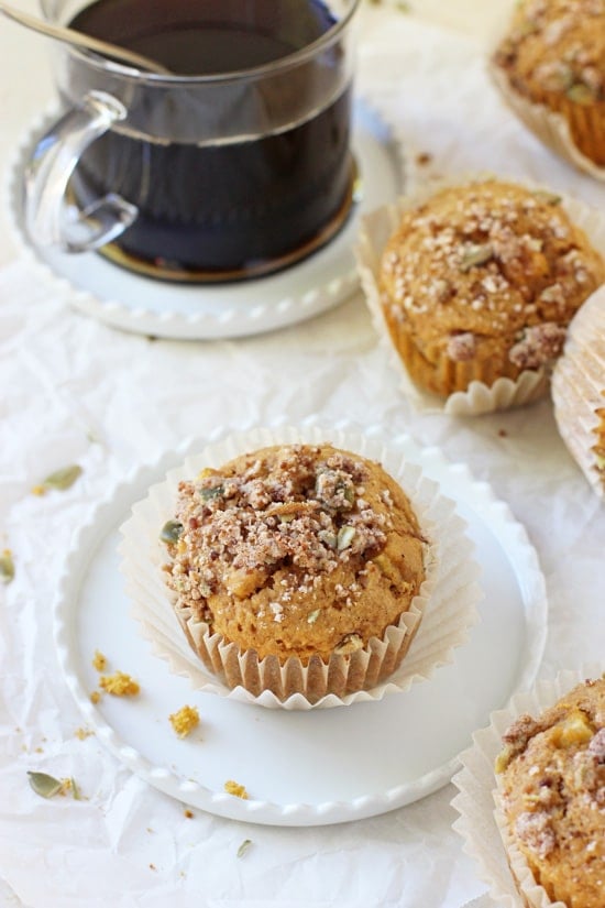 A Harvest Sweet Potato Muffin on a white plate with more muffins plus coffee in the background.