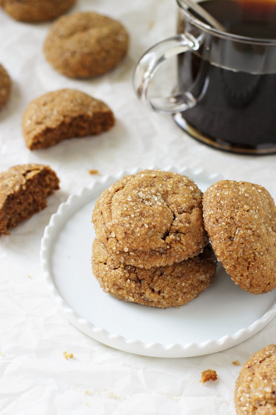 Three Soft & Chewy Whole Wheat Pumpkin Cookies stacked on a plate with more cookies and coffee in the background.