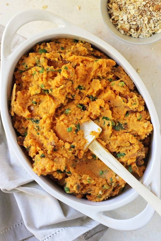 Mashed sweet potato filling spread in a white baking dish with the crumb topping in a bowl to the side.
