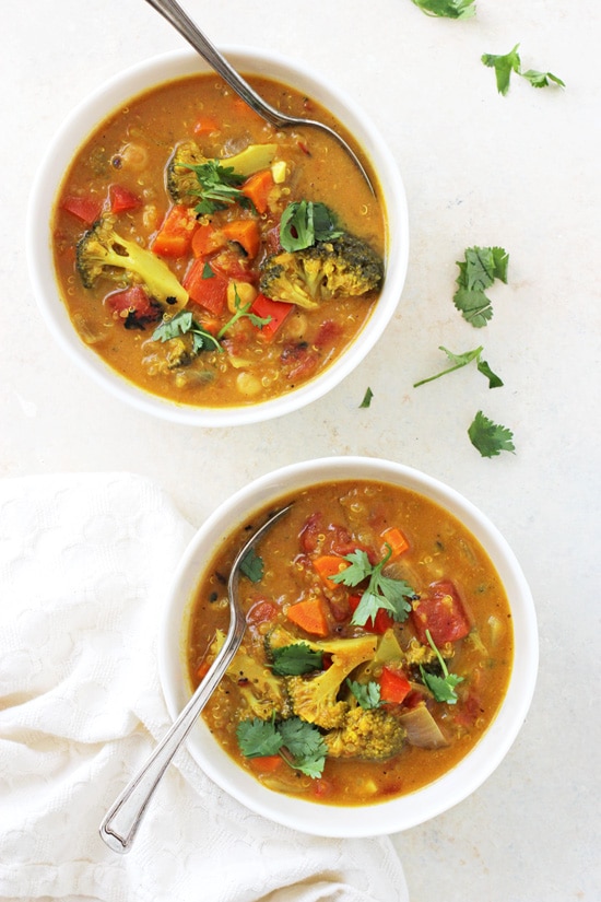 An overhead view of two bowls of Turmeric Quinoa Vegetable Soup with two spoons.