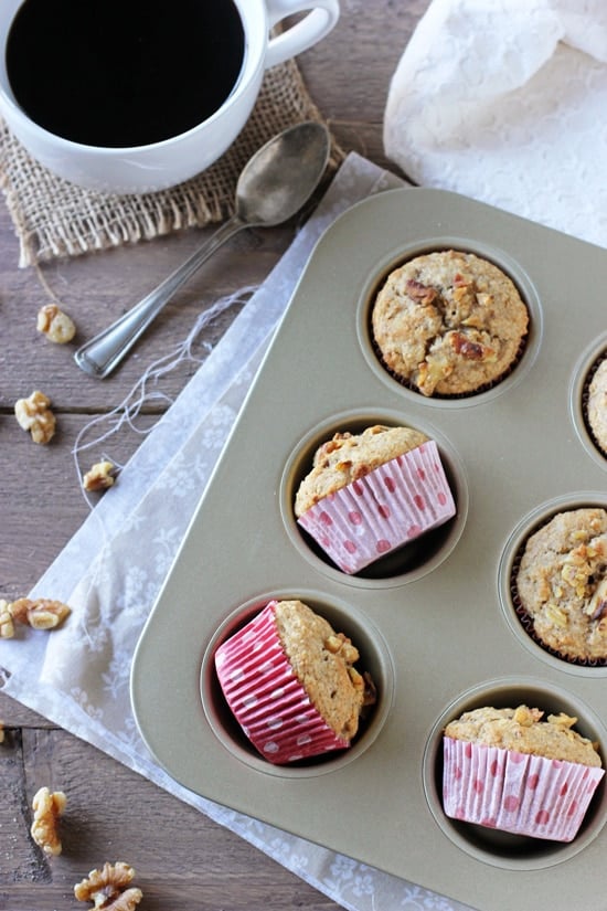 Six Vanilla Cardamom Walnut Muffins in a muffin tin with a cup of coffee to the side.