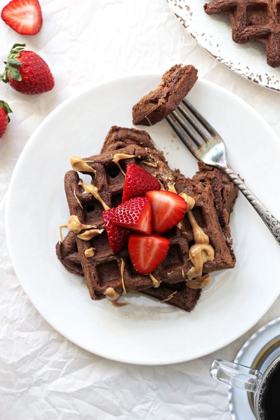 Two Chocolate Whole Wheat Waffles on a plate with strawberries and peanut butter.