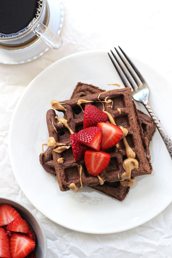 A plate with two Chocolate Whole Wheat Waffles and a bowl of strawberries and coffee off to the side.