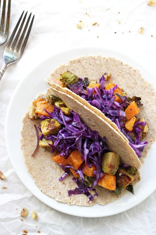 A white plate with two Roasted Winter Vegetable Tacos and two forks to the side.