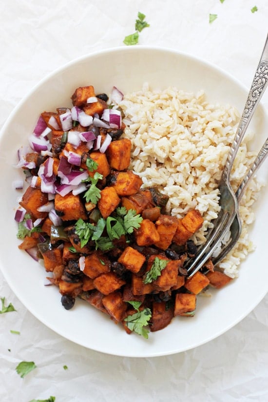 A white bowl filled with Sweet Potato & Black Bean Enchilada Stir-Fry and two forks.