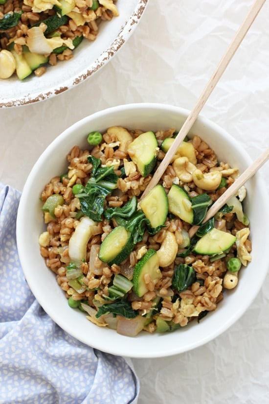 Two white bowls filled with Green Veggie Farro Fried Rice and chopsticks in one bowl.
