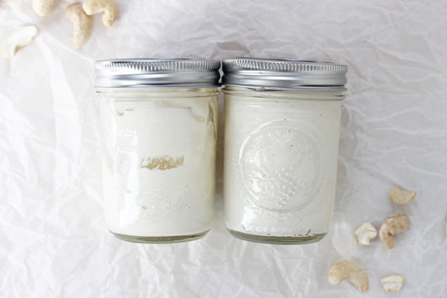 Two glass jars filled with cashew sour cream on white parchment paper.