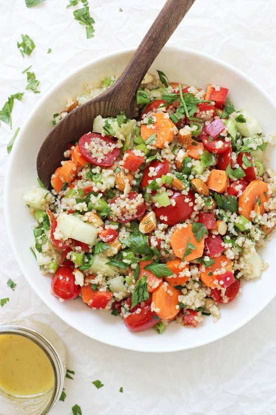 A large bowl filled with Crunchy Summer Veggie Quinoa Salad with a wooden spoon.