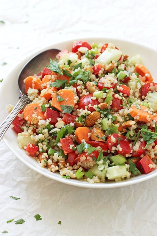 A side angle view of a bowl with Crunchy Summer Veggie Quinoa Salad and a silver serving spoon.