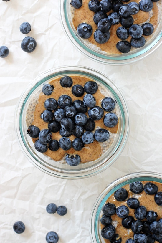 Three small bowls with Blueberry Almond Butter Chia Pudding and blueberries scattered around.