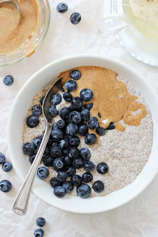 An overhead view of Blueberry Almond Butter Chia Pudding in a bowl with a cup of tea on the side.