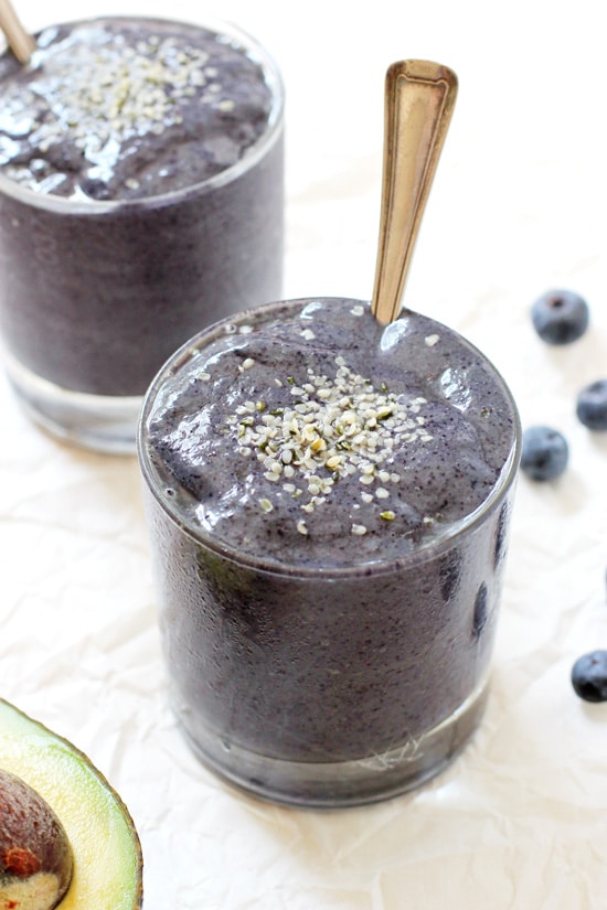 Side angle view of two glasses filled with Blueberry Avocado Protein Smoothie with spoons.