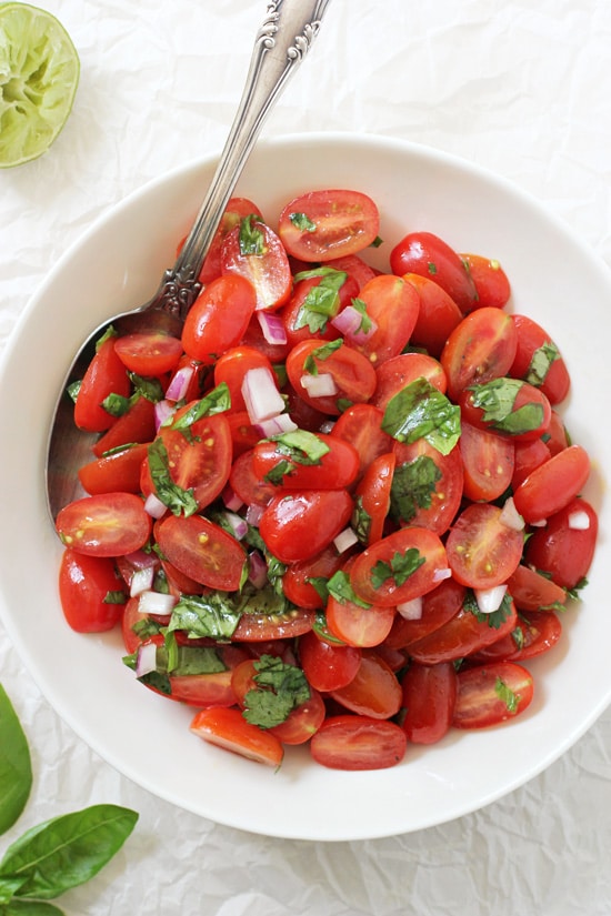 A large white bowl filled with Fresh Cherry Tomato Salsa and a silver serving spoon.