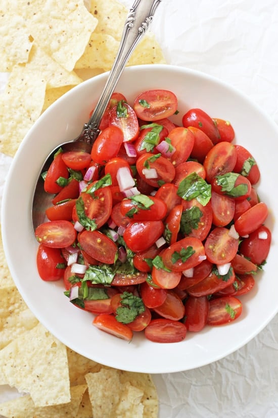 A large bowl filled with Fresh Cherry Tomato Salsa and tortilla chips on the side.