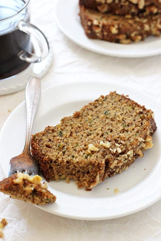 A piece of Orange Poppy Seed Zucchini Bread with a bite taken out and a cup of coffee in the background.