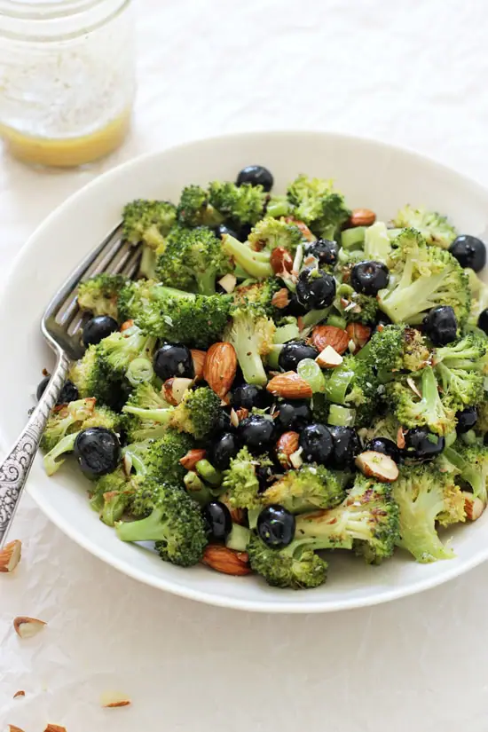 A side angle view of Roasted Broccoli Salad in a white bowl with a fork.