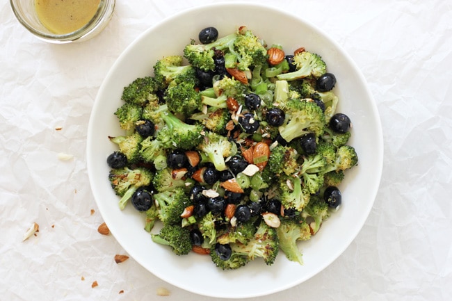 An overhead view of Roasted Broccoli Salad in a white bowl with dressing to the side.