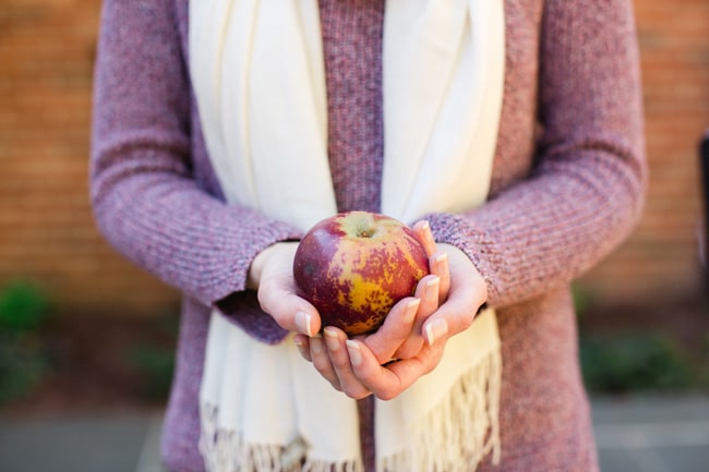 A woman holding a single red apple.