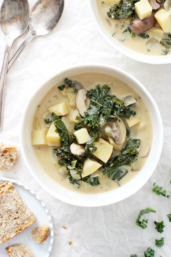 Two bowls of Vegan Zuppa Toscana with a small plate of bread and two spoons.