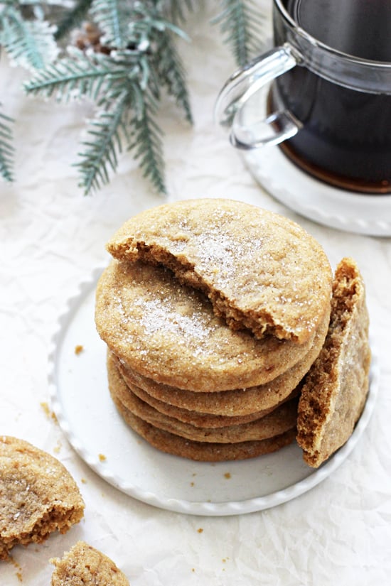 A stack of six Chewy Cardamom Spice Cookies on a white plate with a cup of black coffee in the background.