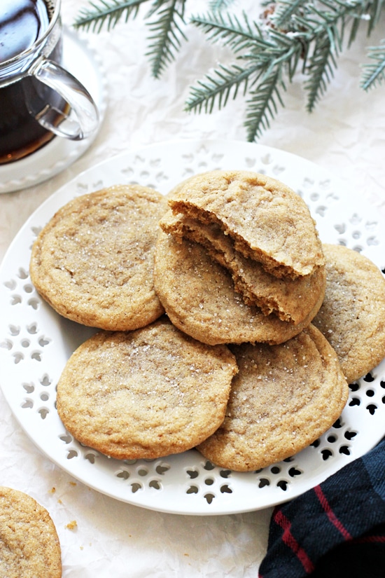 A large white plate filled with Chewy Cardamom Cookies and a cup of coffee in the background.