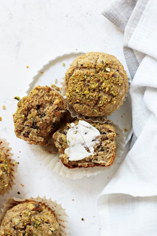 Two Healthier Pistachio Muffins on a plate with one split open and smeared with some butter.