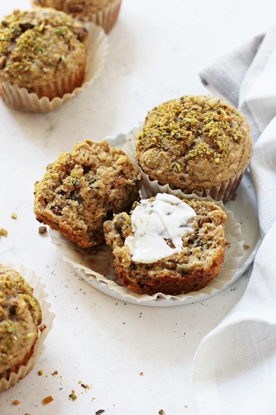 A side angle photo of two Healthier Pistachio Muffins on a small white plate with one split open and topped with butter.