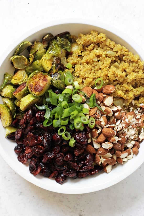 A white bowl filled with roasted brussels sprouts, quinoa, almonds, dried cranberries and green onions.
