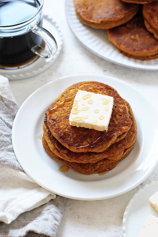 A plate with three Vegan Sweet Potato Pancakes with a pat of butter and coffee in the background.