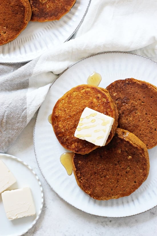 Two white plates with Vegan Sweet Potato Pancakes and pats of butter plus maple syrup.