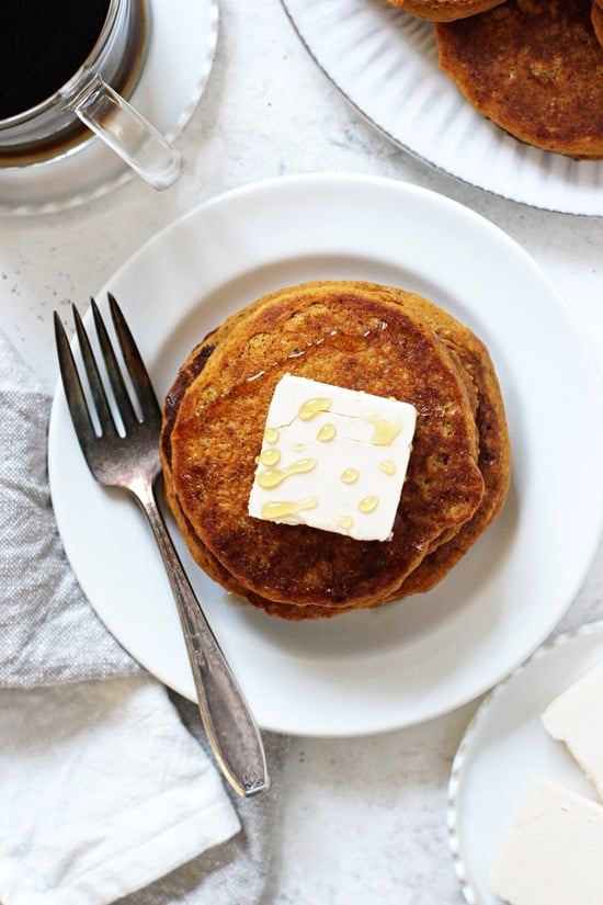 An overhead photo of Vegan Sweet Potato Pancakes on a white plate with coffee and more pancakes in the background.