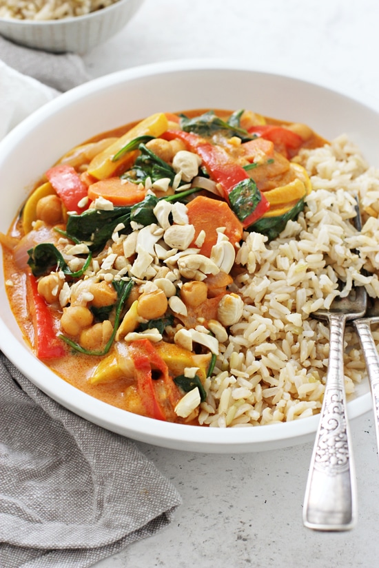 A large white bowl filled with Coconut Chickpea Curry with brown rice and two forks.