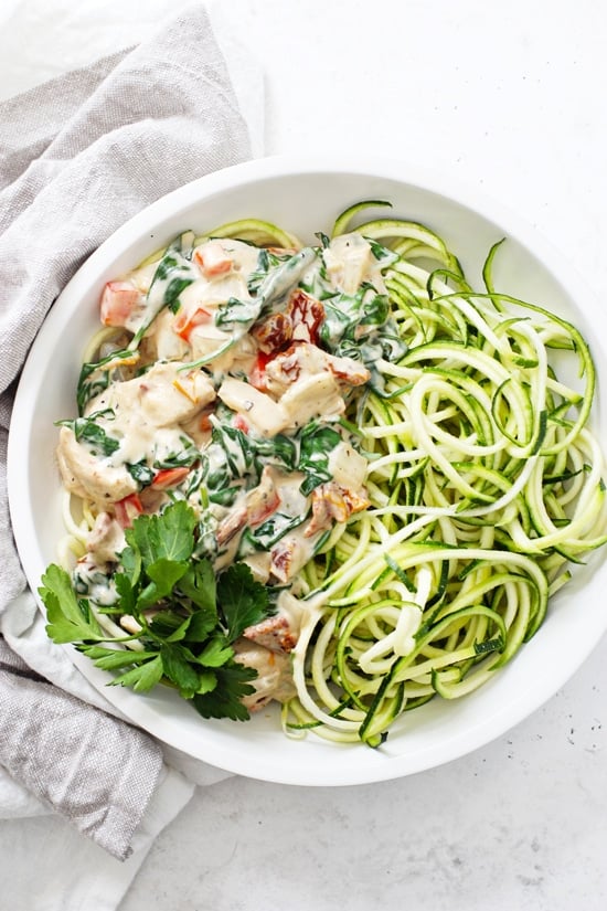 Creamy Tuscan Garlic Chicken in a white bowl with zucchini noodles.