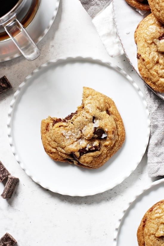 A chewy Mint Chocolate Chip Cookie on a small plate with coffee and more cookies in the background.