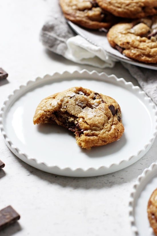 A Mint Chocolate Chip Cookie with a bite taken out of it and a plate of cookies in the background.