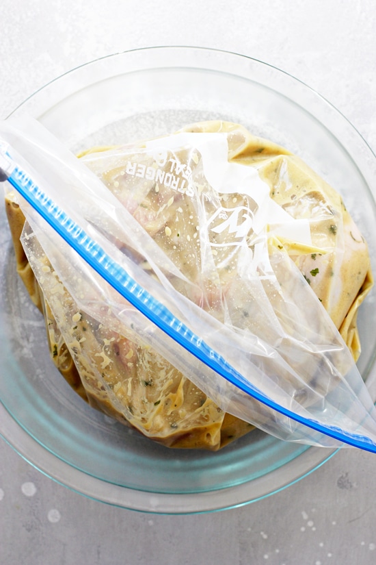 A ziplock baggie filled with marinade and chicken thighs sitting in a glass pie dish.