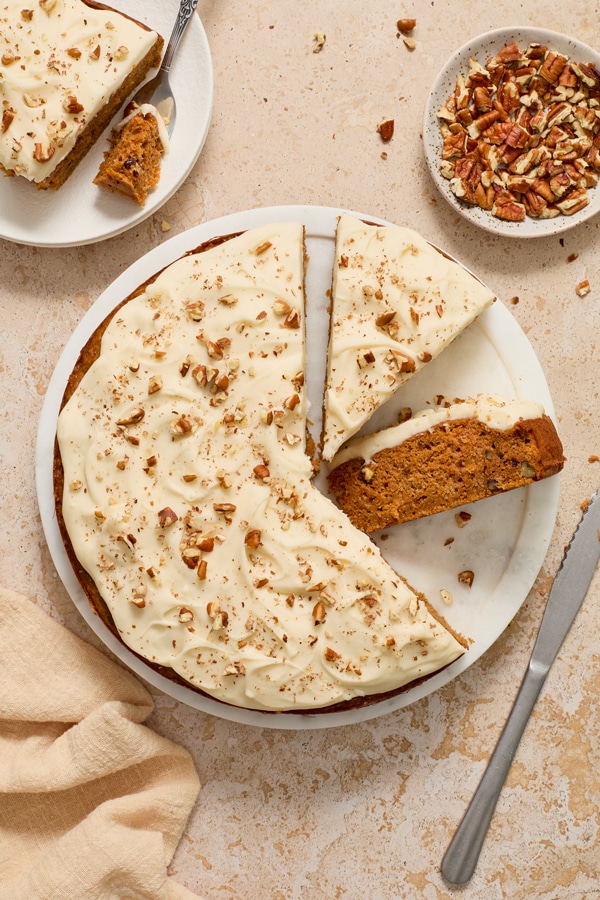 A partially sliced Dairy Free Carrot Cake on a white platter.