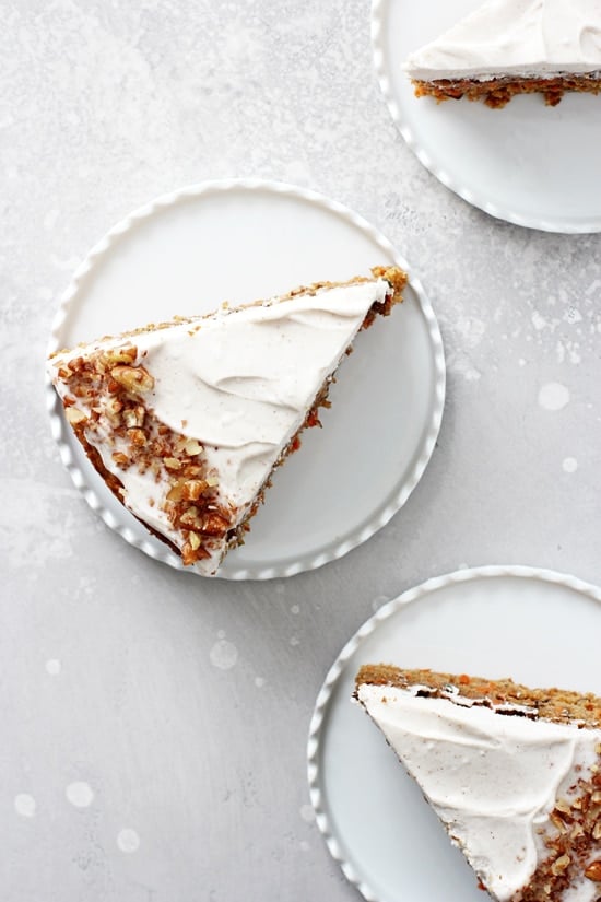 Three slices of Dairy Free Carrot Cake on small white plates on a grey background.
