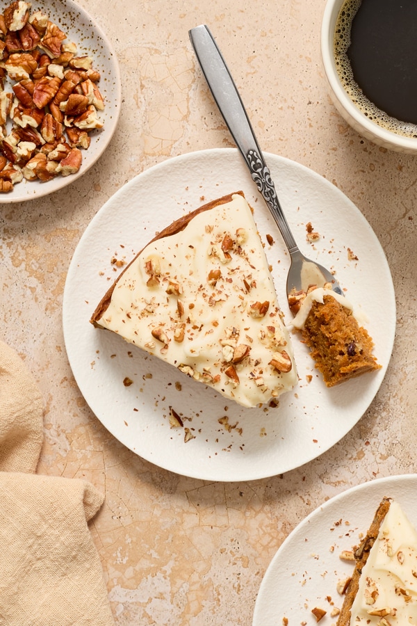 A slice of Dairy Free Carrot Cake on a plate with a bite taken out with a fork.