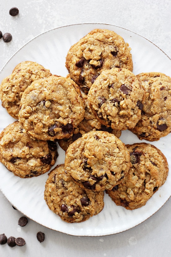 A large white plate filled with Coconut Oil Oatmeal Cookies and chocolate chips scattered around.